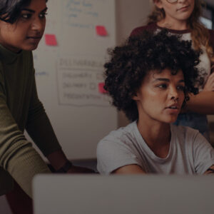 Vier Personen in einem modernen Büro, eine schaut auf einen Computerbildschirm, während die anderen aufmerksam zuschauen.